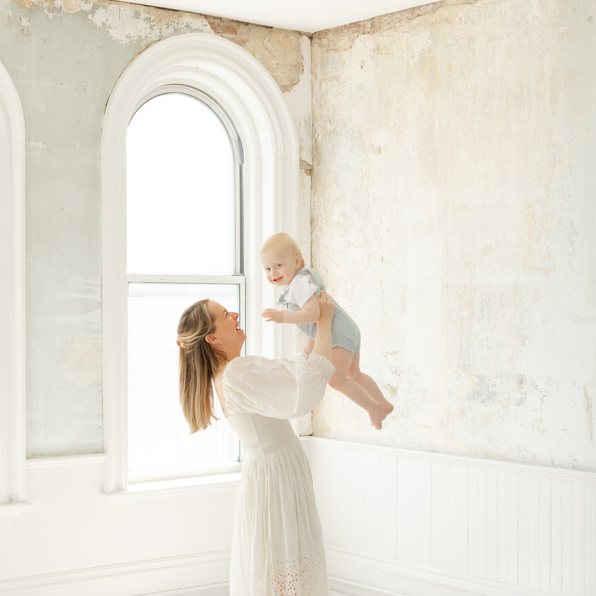 mom wearing cream colored dress lifts up baby boy during boston mini sessions event