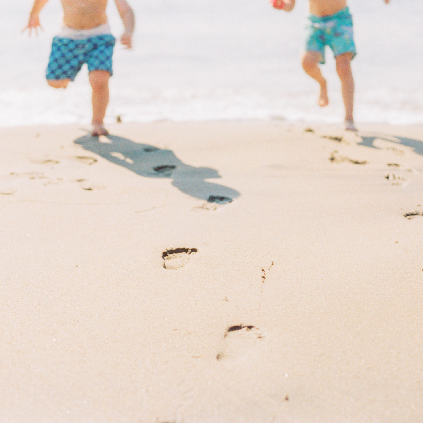 photo of toddlers running on the beach with focus on footprints in the sand