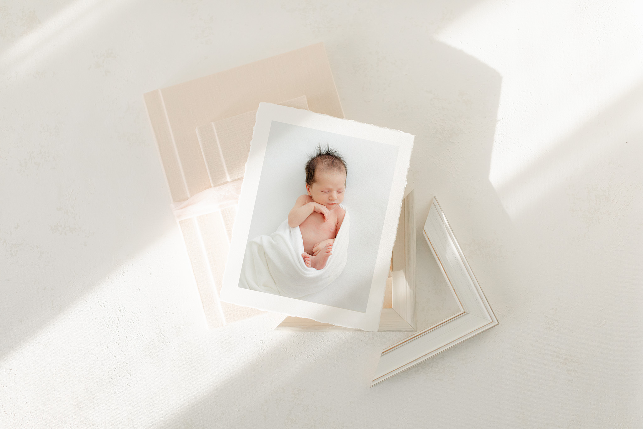 flatlay image of fine art print, album and frame corners showcasing ways to display newborn portraits in your home