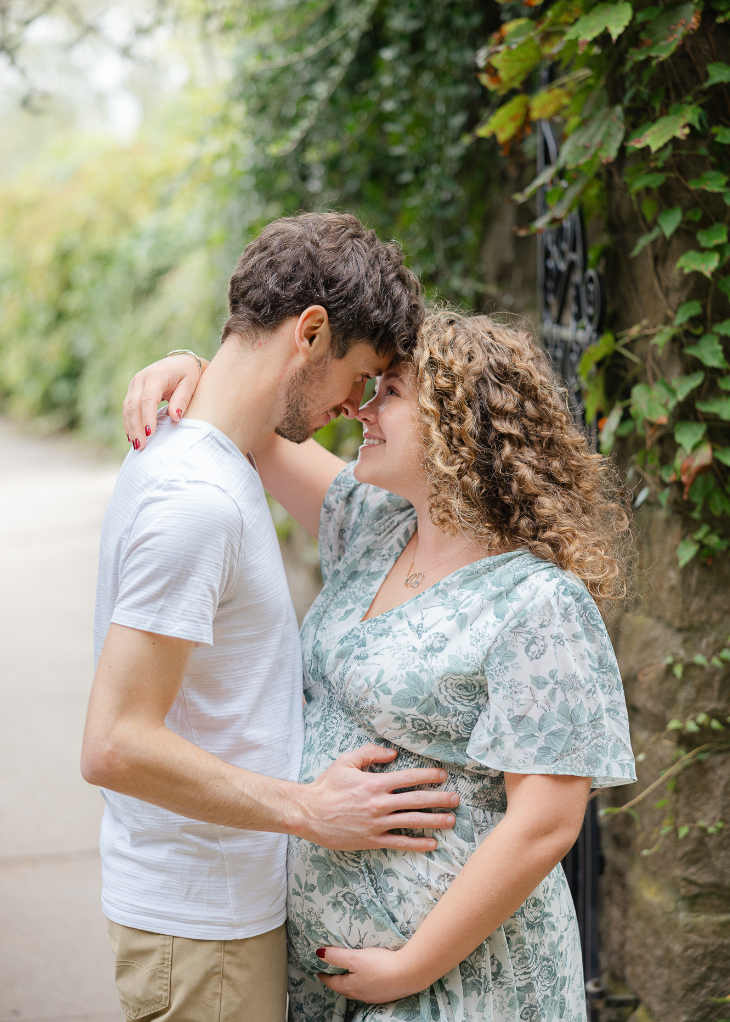 Connecticut maternity photographer captures a tender moment as an expecting couple leans in close, smiling with joy in a lush garden setting.