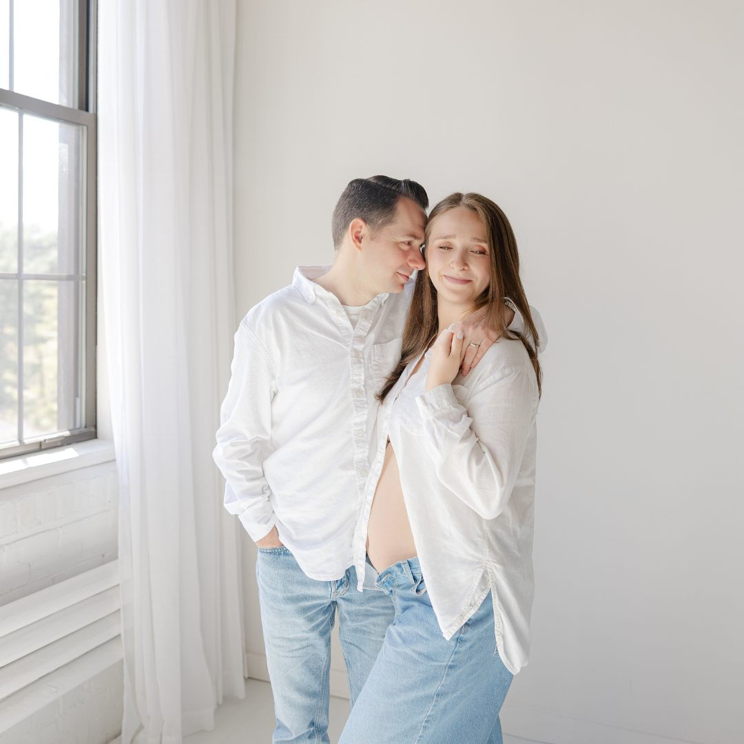 Expectant couple in oversized white shirts during a framingham maternity photographer studio session.